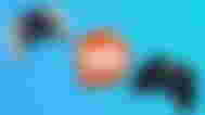 Reddit logo in orange and white, featuring an alien face in the middle, next to a white and black DualSense Edge and a black Razer controller.